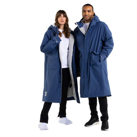 Male and female models wearing admiral blue Slimline Parka robes made by Red Original against a white background. Grey lining, hoods and pockets are also showing.  