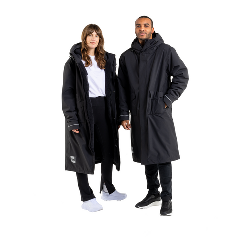 A man and a woman wearing black coloured Red Original Slimline Parka robes with pockets, hoods and external logos against a white background. 