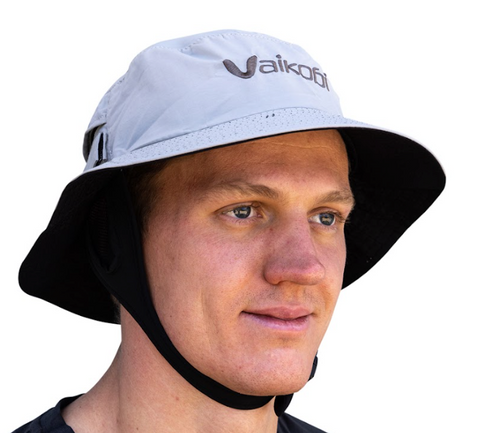 A person wearing a grey Vaikobi Downwind Surf Hat with a wide brim and an adjustable chin strap.